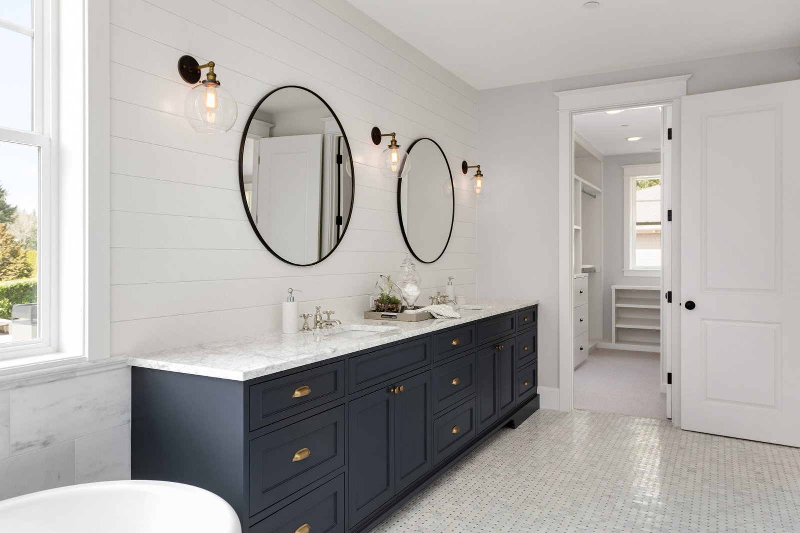 A beautifully renovated bathroom in Asbury Park, NJ with a dark blue vanity along with black hardware, faucet, circular mirrors, and lights.