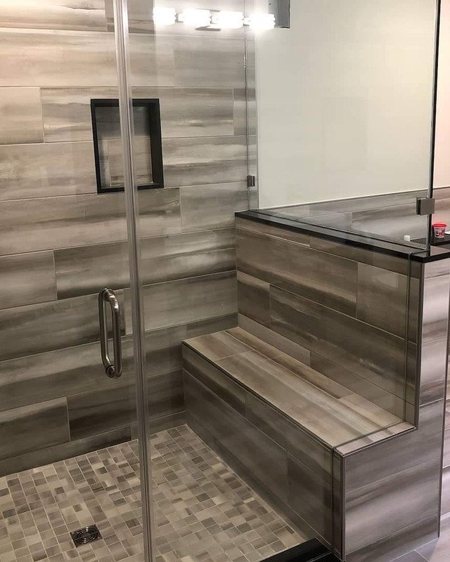 Picture of a large glass enclosed shower in Asbury Park, NJ. The shower has a large bench with large gray tiles.