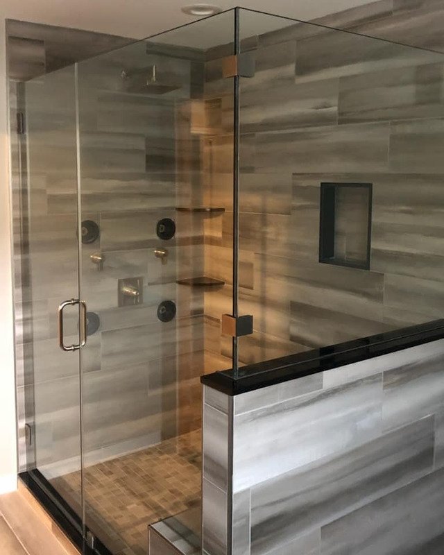 A picture of a modern shower remodel in Asbury Park, NJ. The shower is a sleek look with a glass enclosure. The tile is gray and has black finishes.