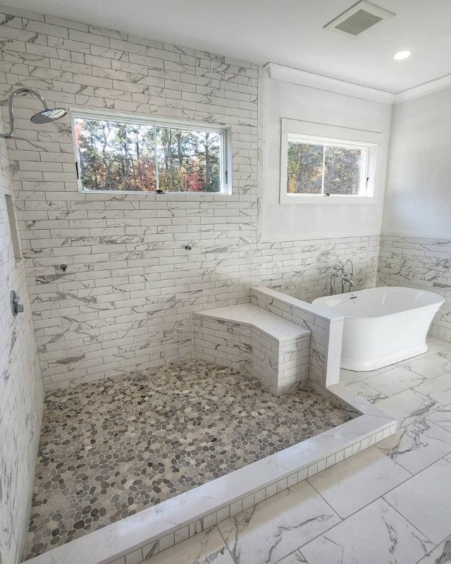 Picture of a renovated bathroom in Asbury Park, NJ. A large walk in shower with a pebble floor and tiled walls is next to a standalone tub.